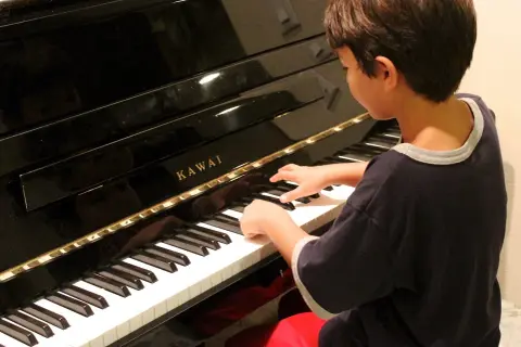 Chłopiec z zapałem gra na pianinie Kawai. Może kiedyś skomponuje własną melodię i powie: "zagraj to sam".