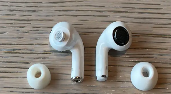 Dwa białe słuchawki AirPods i dwie gumowe nakładki na drewnianym tle.