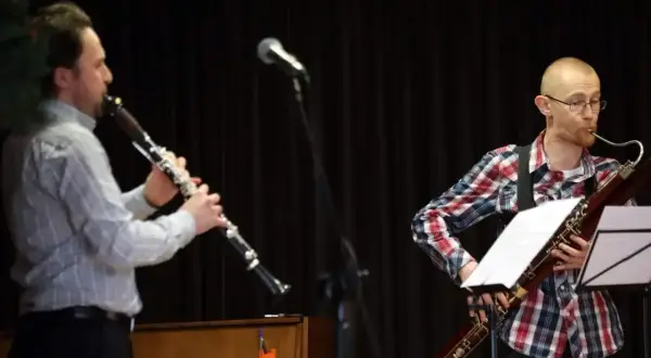Dwóch muzyków gra na instrumentach dętych. Jeden na klarnecie, drugi na fagocie. Przed nimi stoją nuty na klarnet znane piosenki.