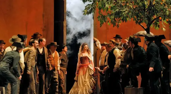 Scena z opery Carmen, gdzie kompozytor Bizet stworzył niezapomnianą postać cyganki. Wokół niej tłum mężczyzn w strojach z epoki.