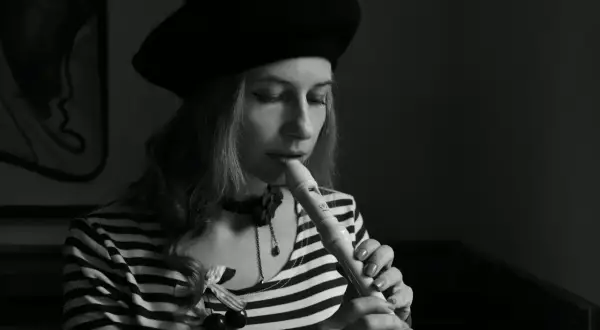 Kobieta w beretce gra na flecie. Pokazuje, jak się gra gamę na flecie, skupiona na melodii.