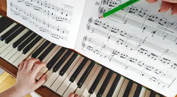 Dziecko gra proste nuty na pianino. Nauczycielka zaznacza ołówkiem fragment utworu.