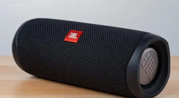 Czarny głośnik JBL Flip leży na drewnianym blacie. Dowiedz się, jak włączyć słuchawki bezprzewodowe JBL, by cieszyć się muzyką.