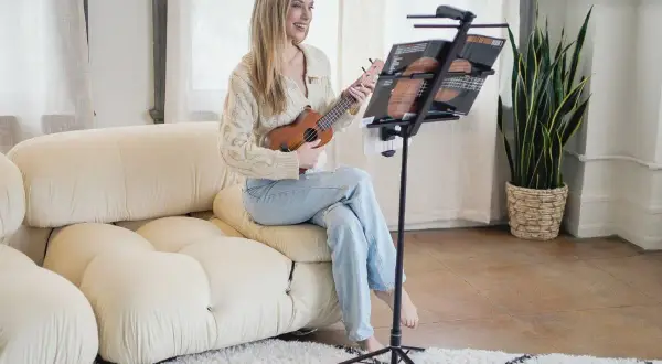 Uśmiechnięta kobieta gra na ukulele, korzystając z podstawki do nut.