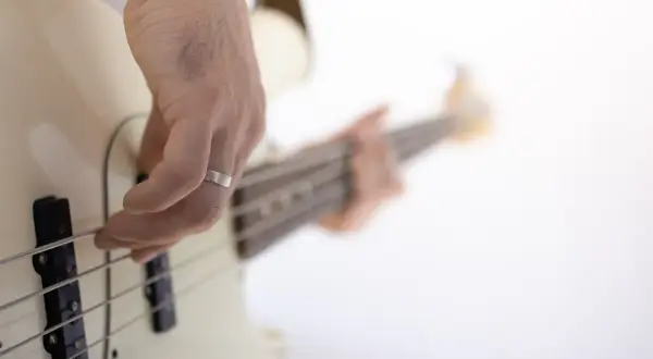 Dłoń z pierścionkiem ćwiczy naukę gry na gitarze basowej, szarpiąc struny.