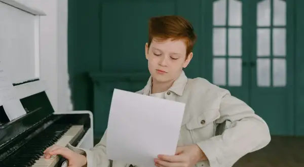 Chłopiec z rudymi włosami ćwiczy grę na pianinie, studiując nuty. Może właśnie poznaje nazwy oktaw, przygotowując się do występu.