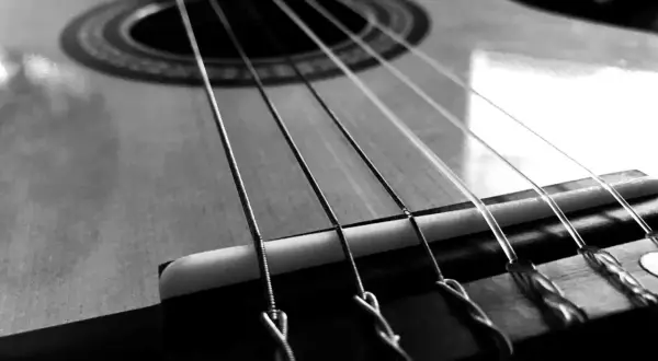 Zbliżenie na gitarę, gdzie widoczne są napięte struny. Ich metaliczny połysk i sposób mocowania przy mostku sugerują gotowość do wydobycia pięknych dźwięków.
