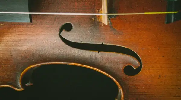 Drewniany korpus skrzypiec z widocznymi strunami. Delikatne rysy na lakierze świadczą o historii instrumentu, który czeka na swoje dźwięki.