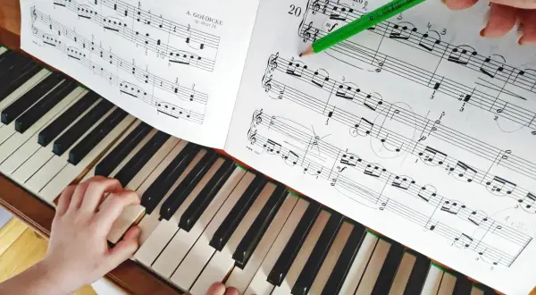 Dziecko uczy się grać proste melodie na pianino. Zielony ołówek wskazuje nuty w zeszycie.