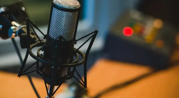 Profesjonalny mikrofon studyjny na statywie, idealny do podcastów. W tle widać sprzęt audio.