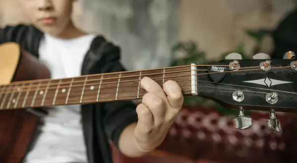 Chłopiec ćwiczy akord d7 na gitarze. Palce układają się na gryfie, gotowe do zagrania kolejnej nuty.