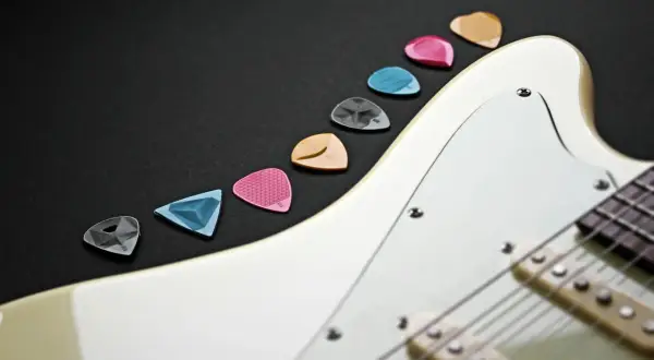 Kolorowe kostki do gitary ułożone wzdłuż białego korpusu instrumentu. Idealne akcesoria, by zacząć naukę gry na gitarze.