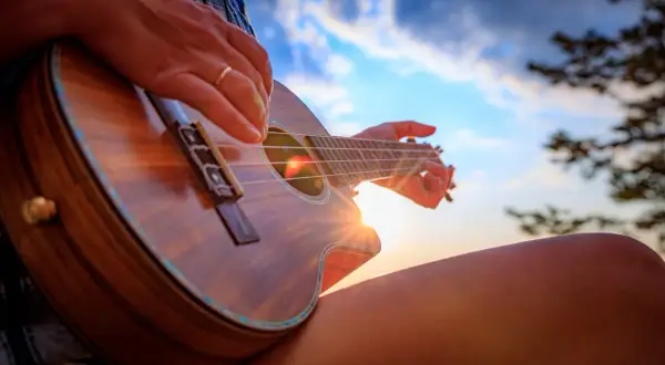 Słońce zachodzi, a ja uczę się, jak się gra na ukulele. Dźwięki instrumentu unoszą się w powietrzu.