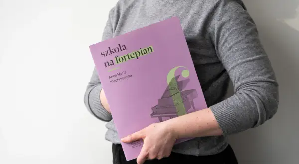Osoba trzyma okładkę "Szkoła na fortepian Klechniowska" z grafiką fortepianu.