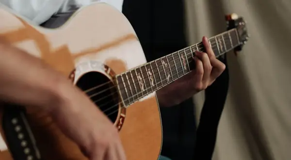 Dłoń grająca na gitarze akustycznej. Zastanawiasz się, ile trwa nauka gry na gitarze? To zależy od Ciebie!