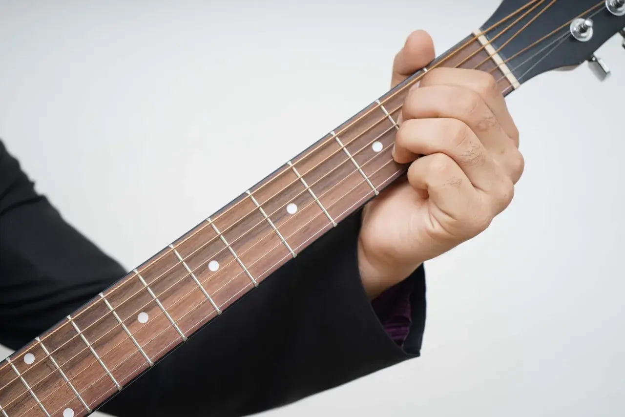Dłoń dociska struny gitary, tworząc akord. Piękna muzyka na gitarę w zasięgu ręki.