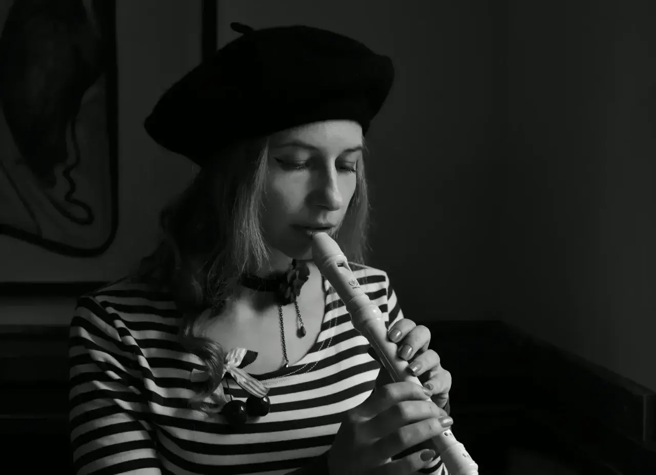 Kobieta w beretce gra na flecie. Pokazuje, jak się gra gamę na flecie, skupiona na melodii.