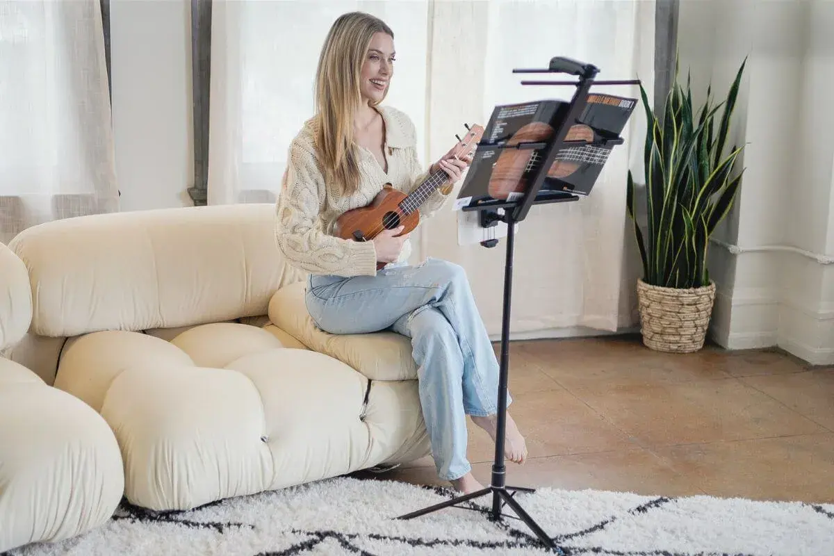 Uśmiechnięta kobieta gra na ukulele, korzystając z podstawki do nut.