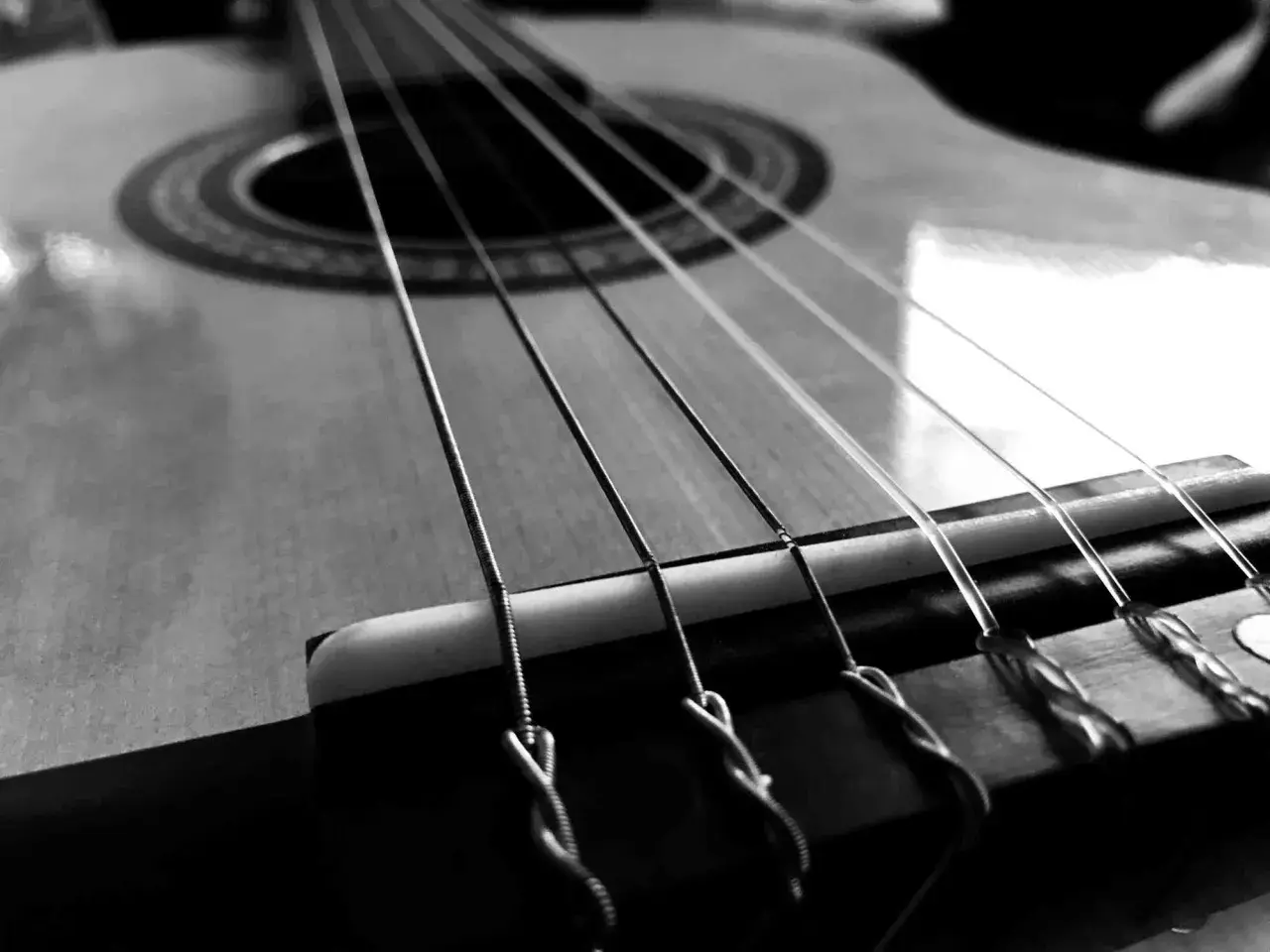 Zbliżenie na gitarę, gdzie widoczne są napięte struny. Ich metaliczny połysk i sposób mocowania przy mostku sugerują gotowość do wydobycia pięknych dźwięków.