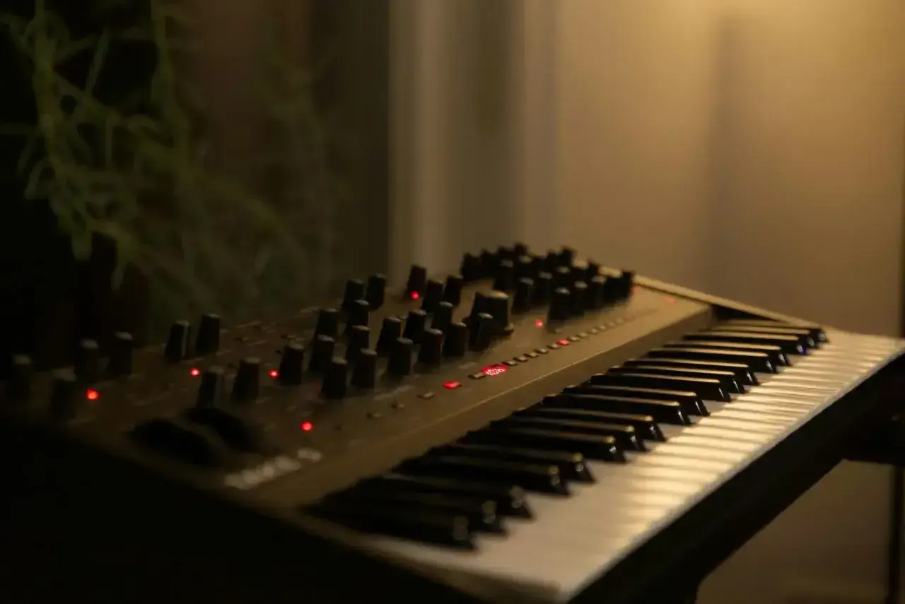 Ciemny, nowoczesny elektroniczny instrument klawiszowy z wieloma pokrętłami i czerwonymi diodami.