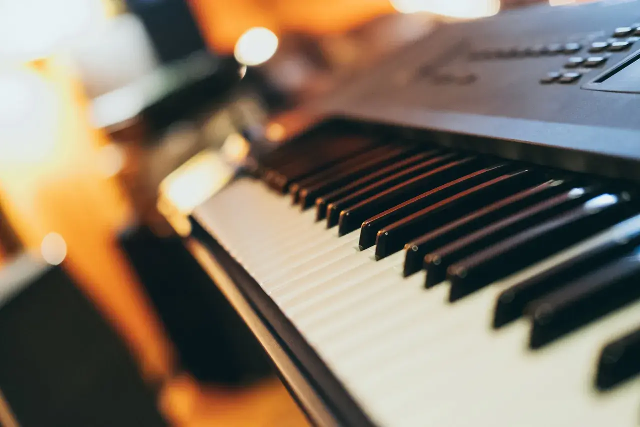 Klawiatura keyboardu, gotowa do zagrania popularnych piosenek. Ciepłe światło otoczenia tworzy przytulną atmosferę.
