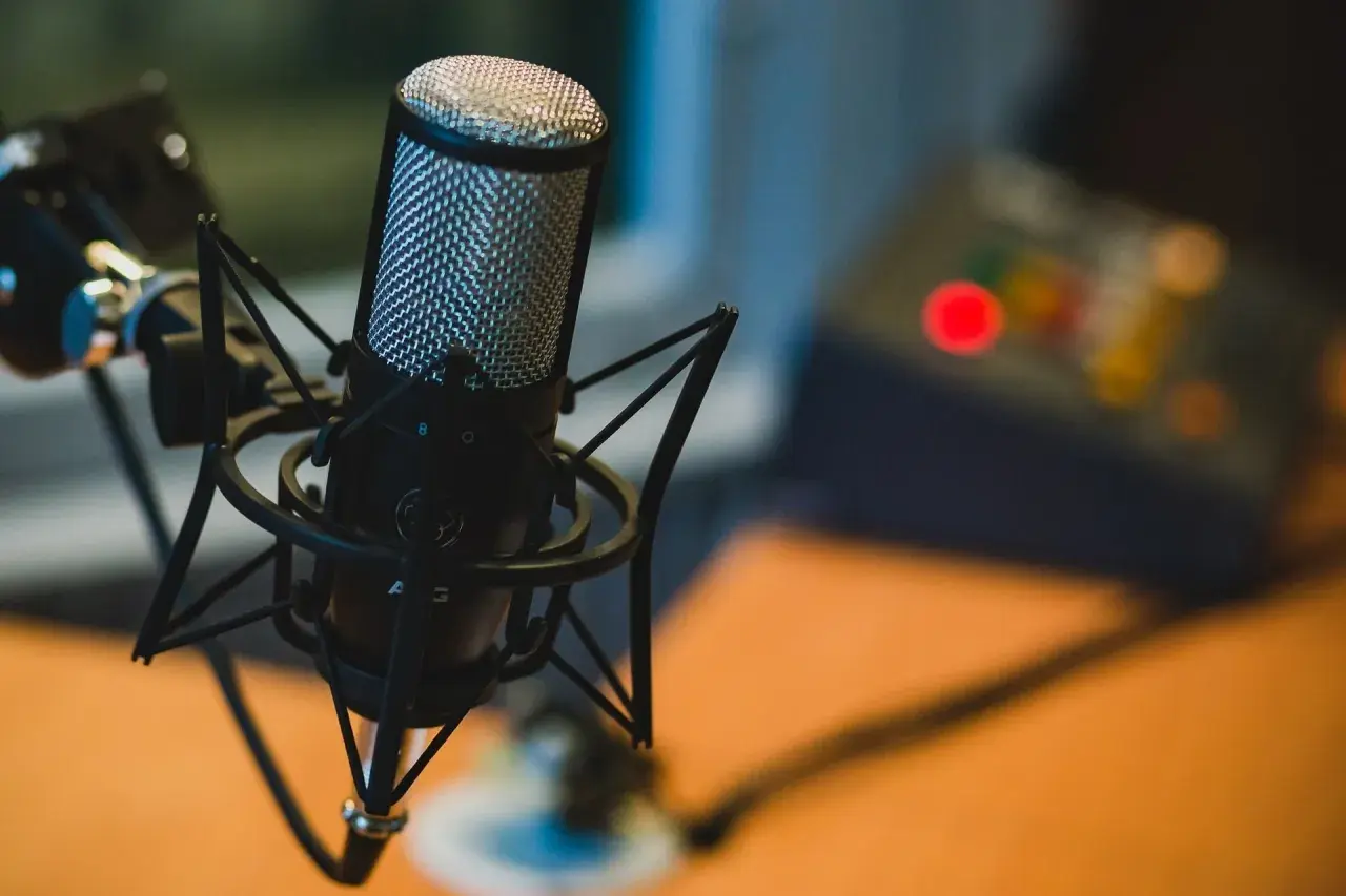 Profesjonalny mikrofon studyjny na statywie, idealny do podcastów. W tle widać sprzęt audio.
