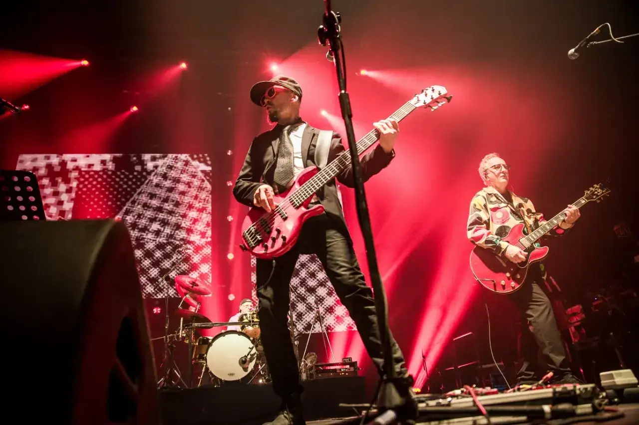 Zespół Lady Pank, autorzy ścieżki dźwiękowej do filmu Kiler, na koncercie. Muzycy grają na gitarach w czerwonych światłach.