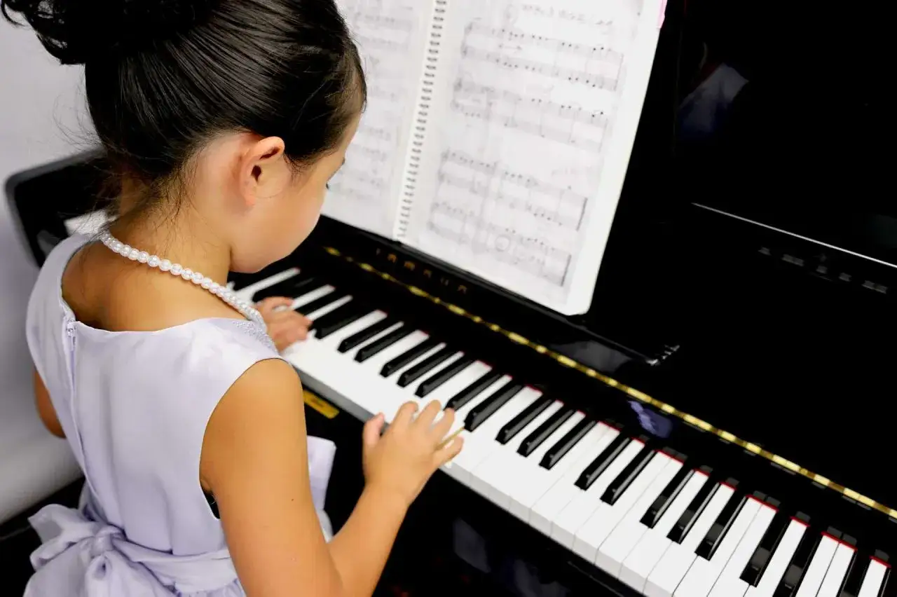 Dziewczynka w białej sukience ćwiczy proste melodie na pianino dla dzieci, patrząc na nuty.