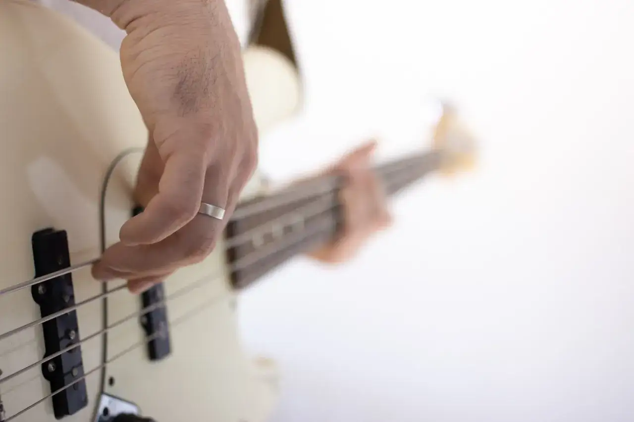 Dłoń z pierścionkiem gra na białej gitarze basowej. Nauka gry na basie to świetna przygoda.