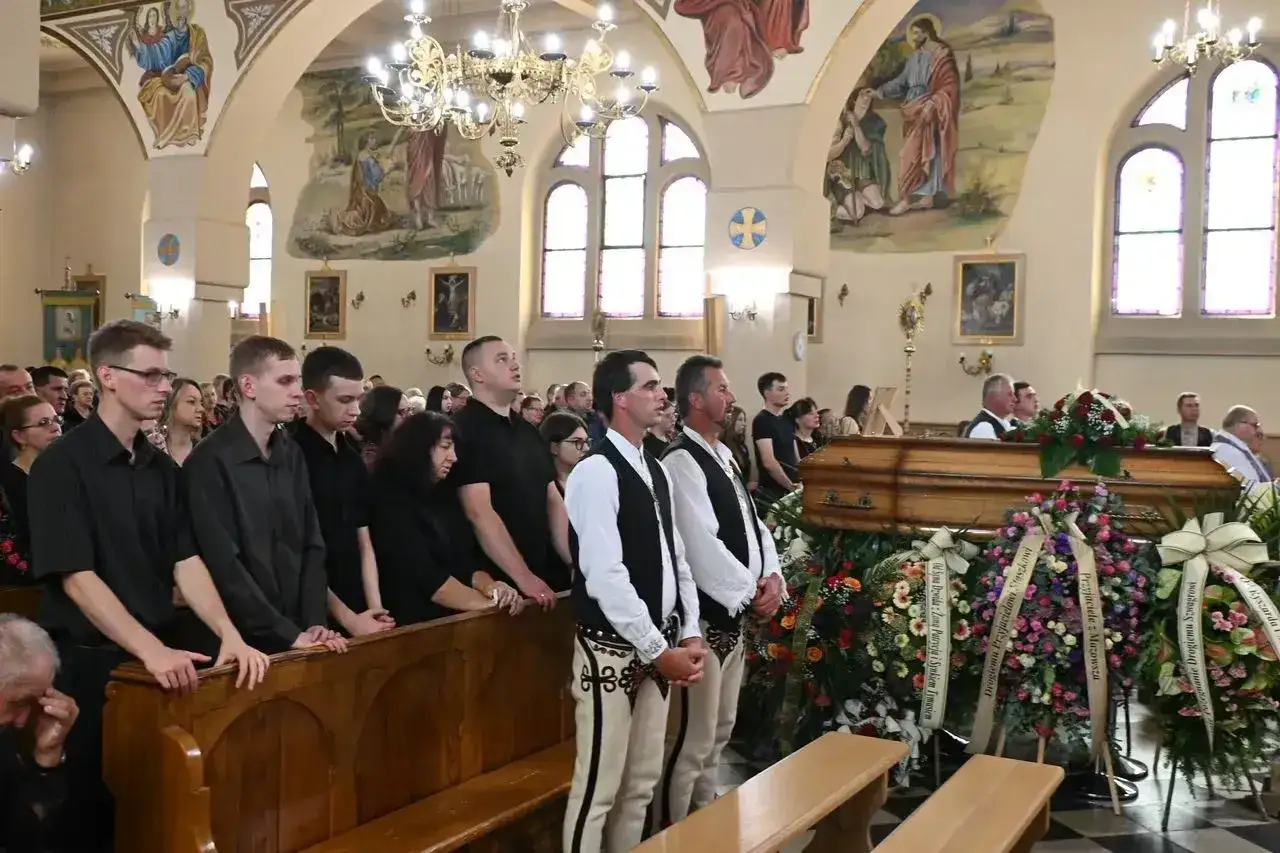 W kościele trwa pogrzeb. Widać trumnę, wieńce i żałobników. W tle malowidła religijne, a z organów płynie marsz pogrzebowy.