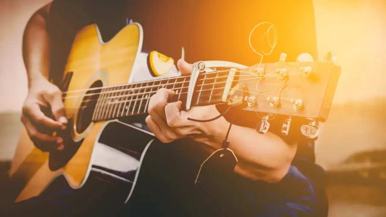 Ręce grające na gitarze klasycznej, uchwycone w ciepłym, słonecznym świetle. To idealny moment na naukę gry na gitarze klasycznej.