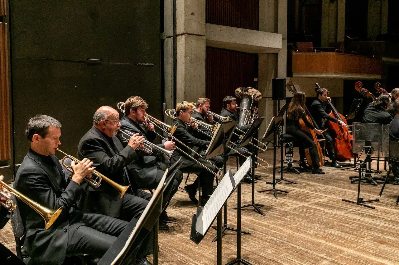 Orkiestra gra na instrumentach dętych blaszanych. Widać trąbki, puzony i tubę.