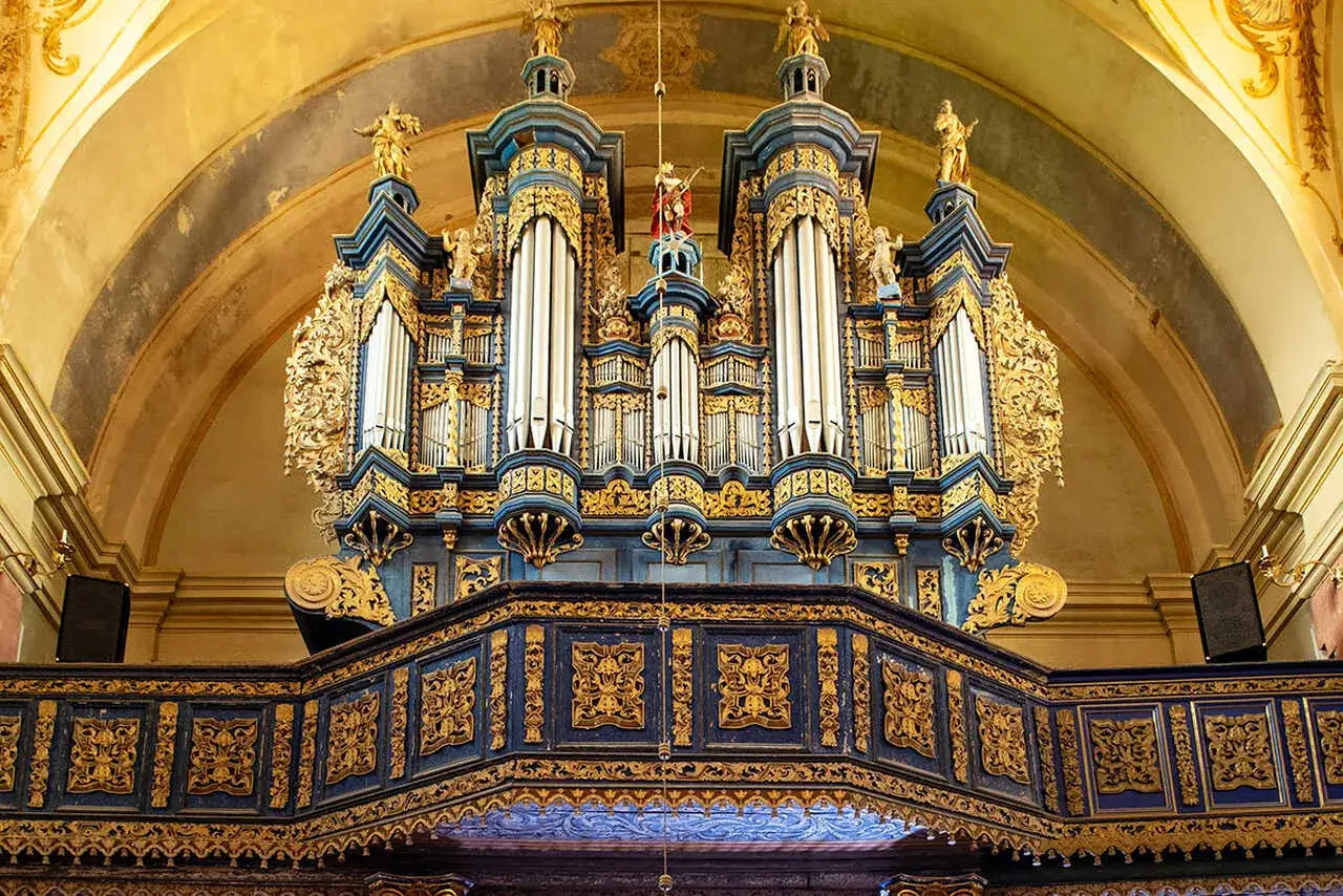 Majestatyczny utwór na organy, ozdobiony złotymi ornamentami i figurkami, góruje nad wnętrzem kościoła.