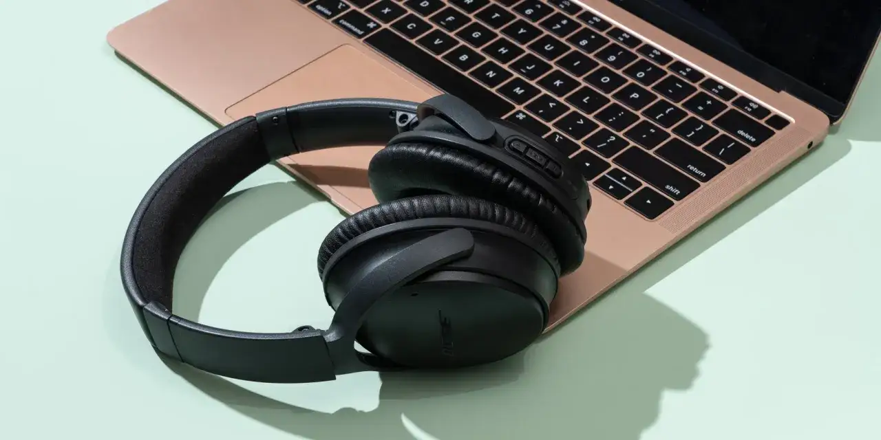 Czarne słuchawki bezprzewodowe Bose leżą obok różowego laptopa. Dowiedz się, jak podłączyć słuchawki bezprzewodowe z laptopem.