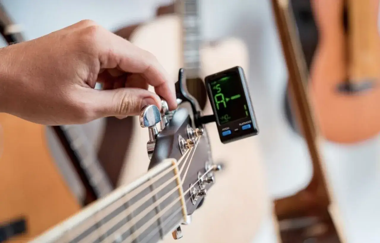 Dłoń kręci kluczem, strojąc gitarę elektryczną. Na ekranie tunera widnieje litera 