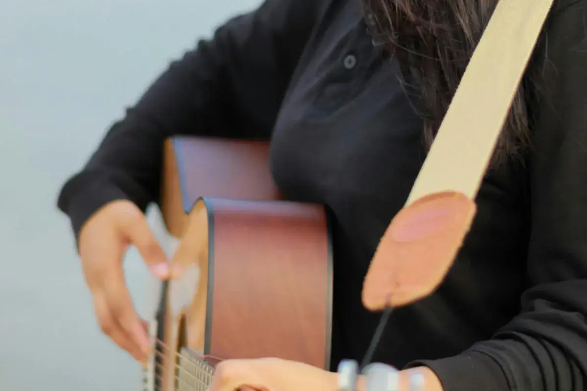 Osoba grająca na gitarze akustycznej, z widocznym paskiem. Pokazuje, jak przyczepić pasek do gitary, by wygodnie grać.
