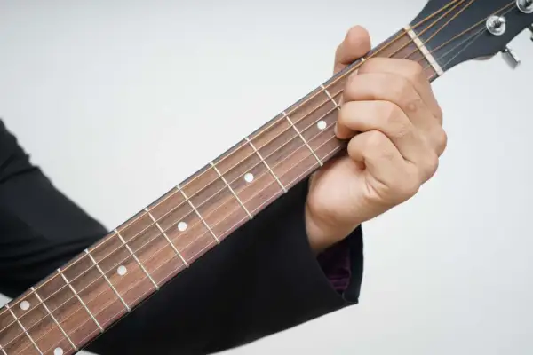 Dłoń dociska struny gitary, tworząc akord. Piękna muzyka na gitarę w zasięgu ręki.