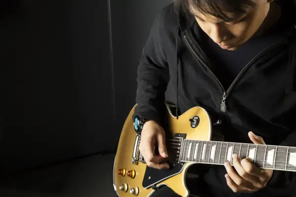 Młody gitarzysta z kostką w dłoni pokazuje, jak trzymać kostkę od gitary, grając na złotej gitarze elektrycznej.