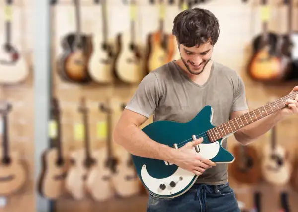 Młody mężczyzna wybiera **jaką gitarę elektryczną na początek** w sklepie muzycznym.