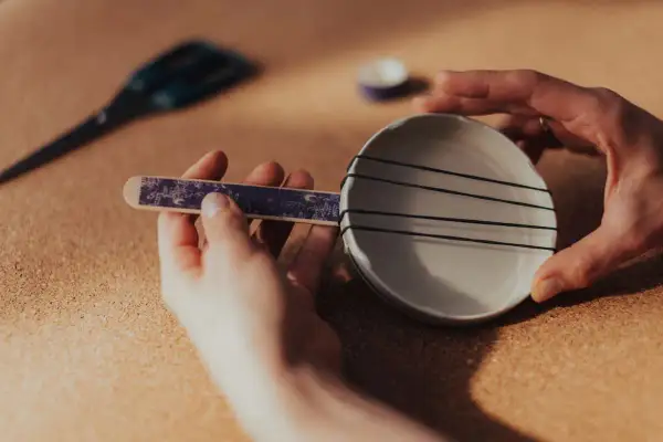 Ręce składają prosty instrument perkusyjny: patyczek z ozdobnym papierem i miseczka z gumkami. Oto jak zrobić instrument perkusyjny!