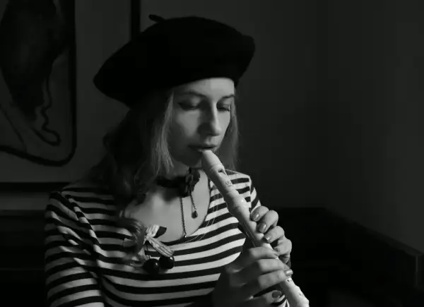 Kobieta w beretce gra na flecie. Pokazuje, jak się gra gamę na flecie, skupiona na melodii.
