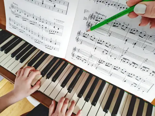 Dziecko gra proste nuty na pianino. Nauczycielka zaznacza ołówkiem fragment utworu.
