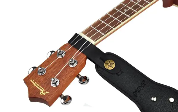 Czarny pasek do gitary przymocowany do gryfu ukulele. Pokazuje, jak przyczepić pasek do gitary, zaczepiając go o główkę instrumentu.