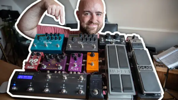 Uśmiechnięty mężczyzna pokazuje swoją bogatą kolekcję efektów gitarowych, prezentując ich kolejność na pedalboardzie.