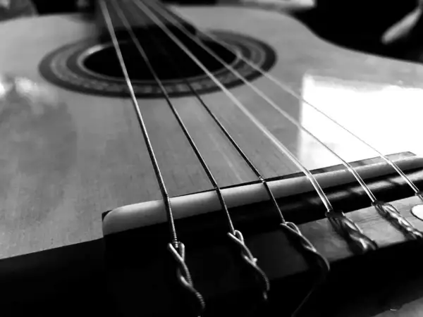 Zbliżenie na gitarę, gdzie widoczne są napięte struny. Ich metaliczny połysk i sposób mocowania przy mostku sugerują gotowość do wydobycia pięknych dźwięków.