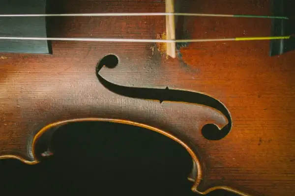 Drewniany korpus skrzypiec z widocznymi strunami. Delikatne rysy na lakierze świadczą o historii instrumentu, który czeka na swoje dźwięki.