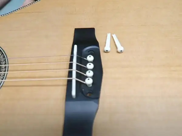 Jak zmienić struny w gitarze klasycznej? Widok na mostek gitary z naciągniętymi strunami i dwoma wyjętymi kołeczkami.