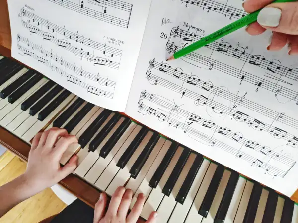 Dziecko uczy się grać proste melodie na pianino. Zielony ołówek wskazuje nuty w zeszycie.