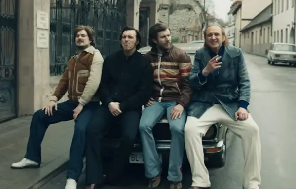 Czterech mężczyzn w stylu lat 70. siedzi na samochodzie. Jeden z nich pali papierosa, przypominając scenę z filmu "Jak pokochałam gangstera".
