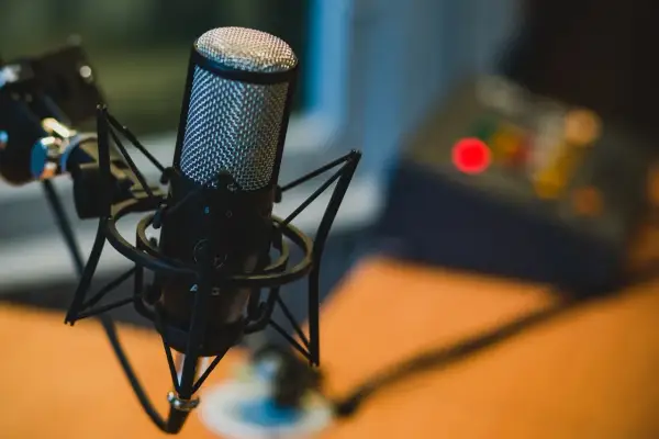 Profesjonalny mikrofon studyjny na statywie, idealny do podcastów. W tle widać sprzęt audio.